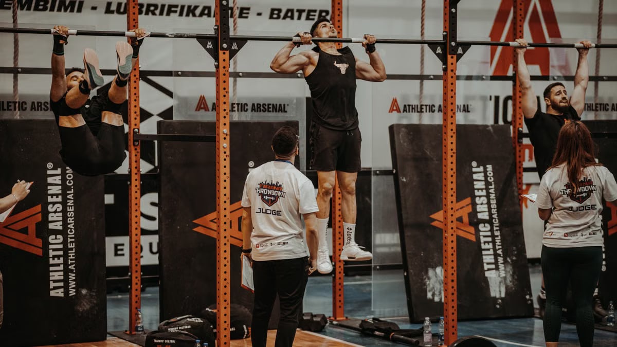 Athletes performing pull-ups in a CrossFit competition, judged by officials, showcasing strength and endurance.